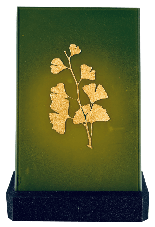 Grüne Glasplatte mit goldenen Blattmotiven, elegant und dekorativ auf schwarzem Sockel platziert.