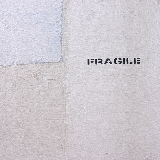 Graffiti auf Mauer mit dem Wort Fragile in Schwarz. Minimalistisches Design auf grober Textur.